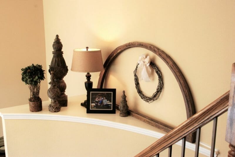 Stairway landing that is decorated with DIY barbed wire wreath, finials and an old window frame
