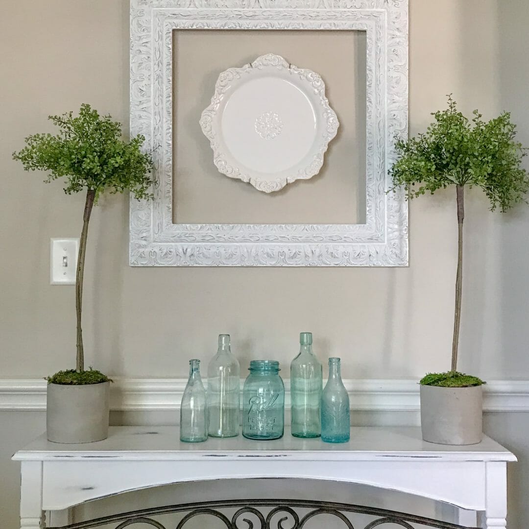 topiaries on table with blue bottles and plate on wall