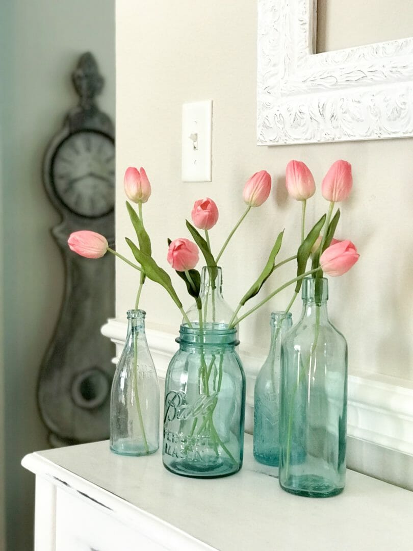 vintage blue bottle collection with pink flowers and floor clock in background leaning against the wall