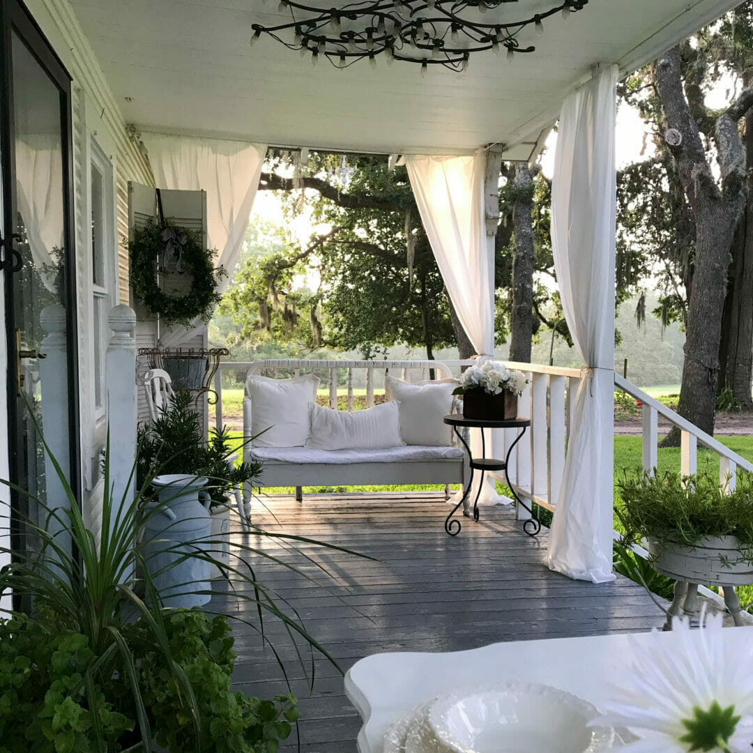 porch with white curtains, plants and a bench with white pillows