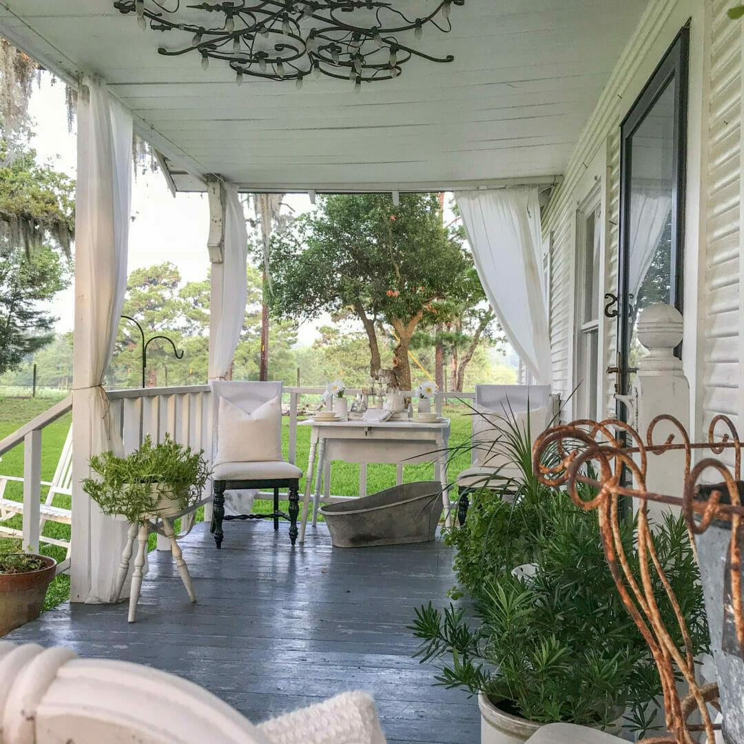 Front porch with plants, iron pieces and vintage tableSummer farmhouse front porch by CountyRoad407.com