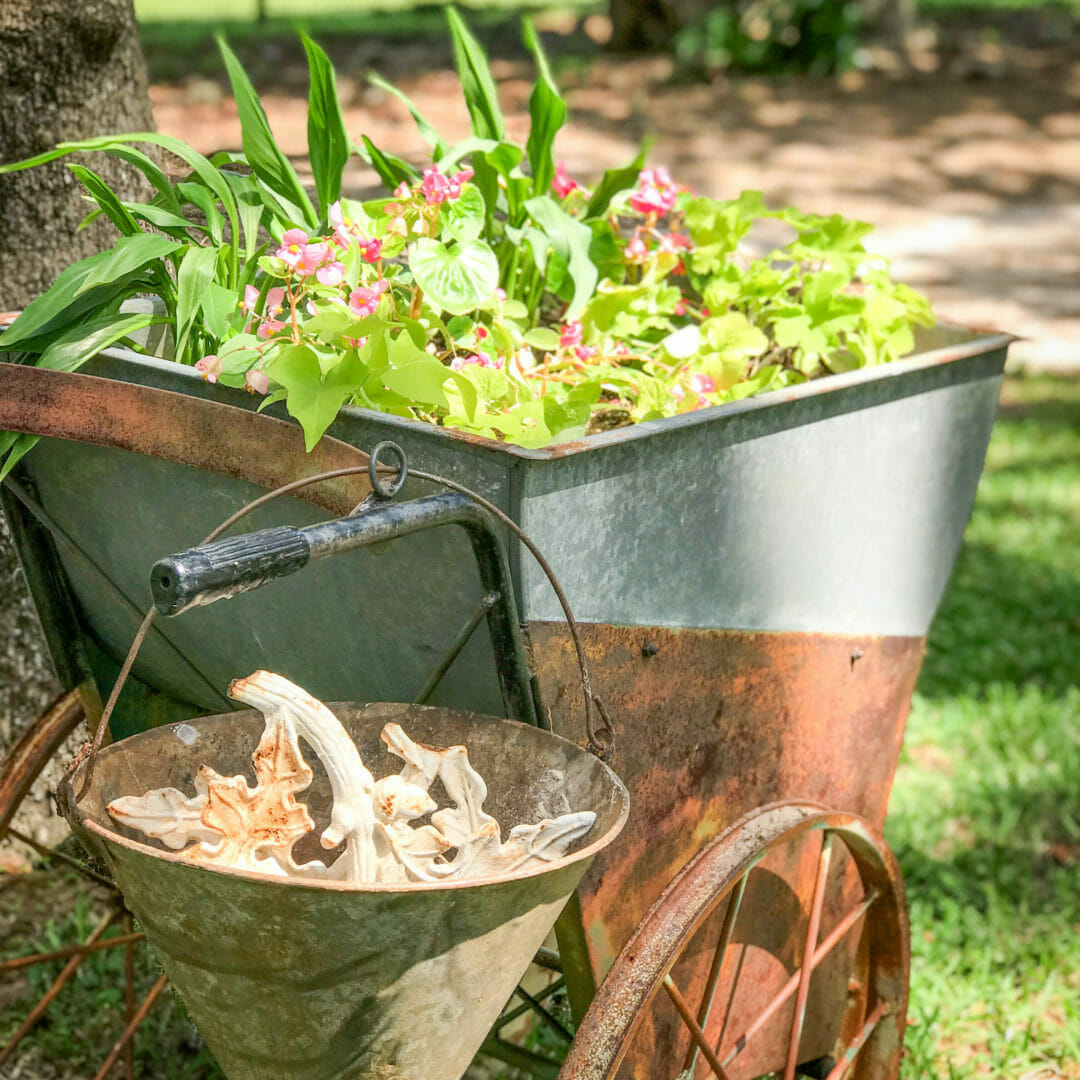 large galvanized cart with plants and a hanging fire bucket on the handleVintage cart used to hold plants by CountyRoad 407.com. Antique cart