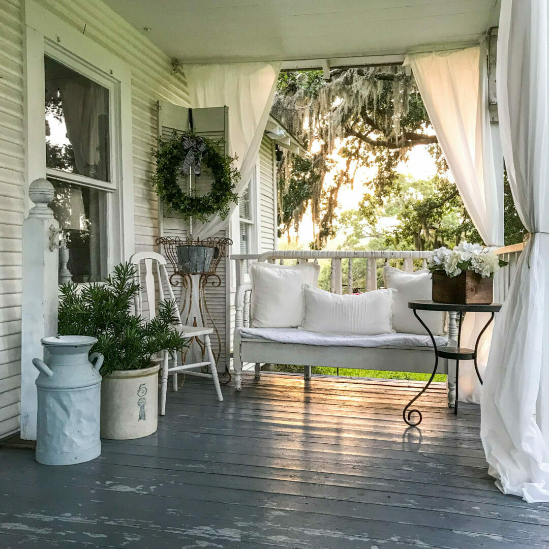 Porch with bed bench, white curtains and plants for a do what you want decorating attitude.