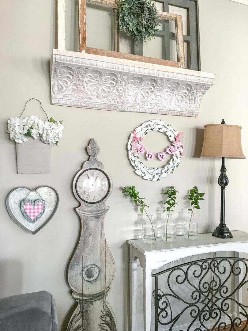 wall with valentine items, clock, wreath, 3 jars with fresh stems, lamp and console table