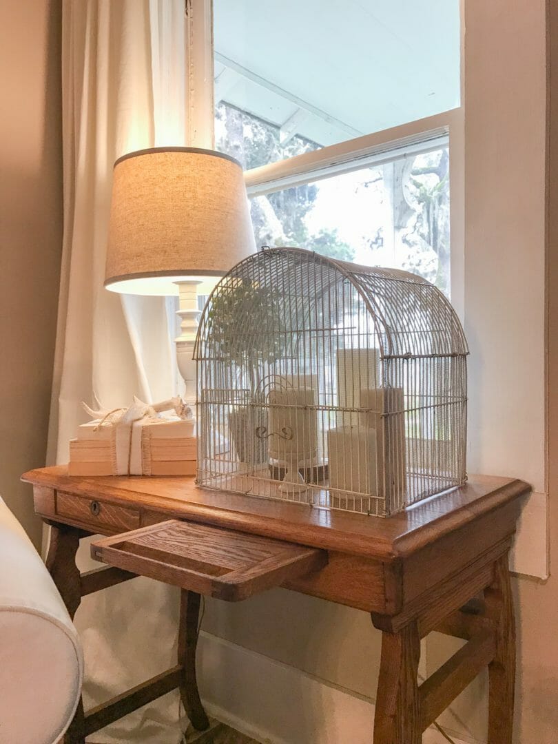 white chair with side table with birdcage cloche and white candles with lamp