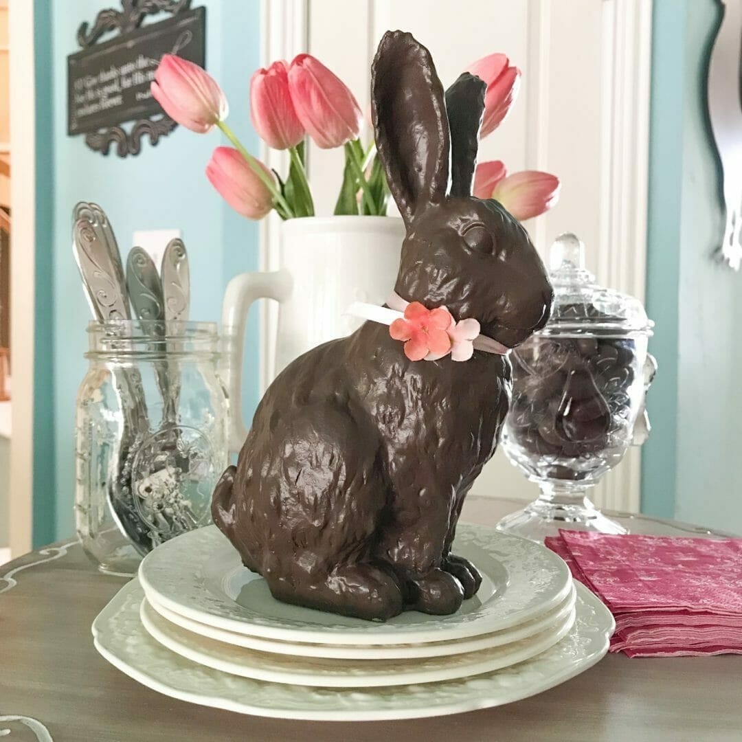 chocolate looking bunny sitting on plates with pink flowers in background