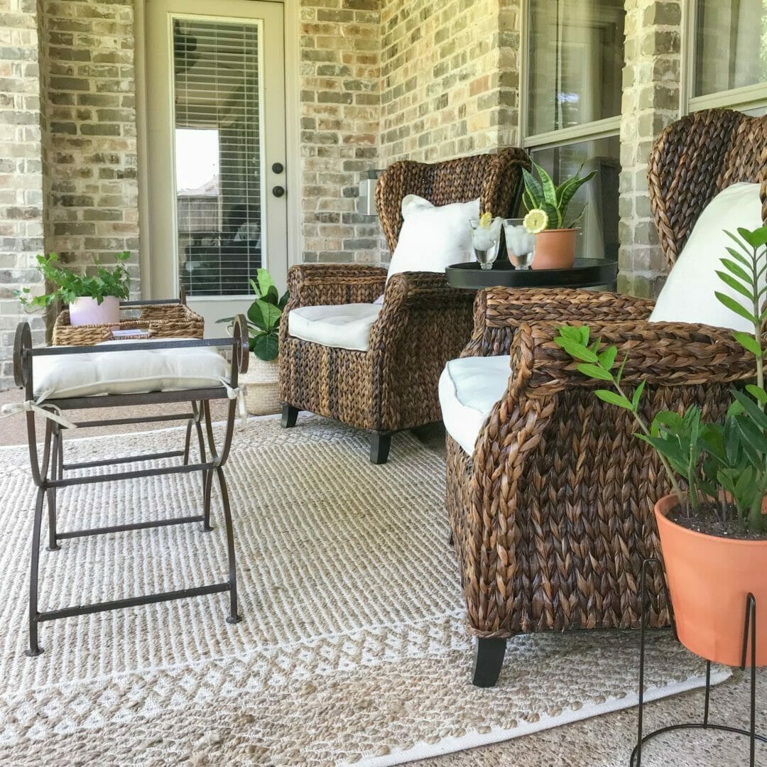 Back porch with dark wicker chairs, rug and metal coffee table and plants