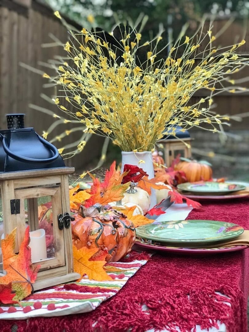 fall table with dishes lantern pumpkins leaf garland and floral arrangement