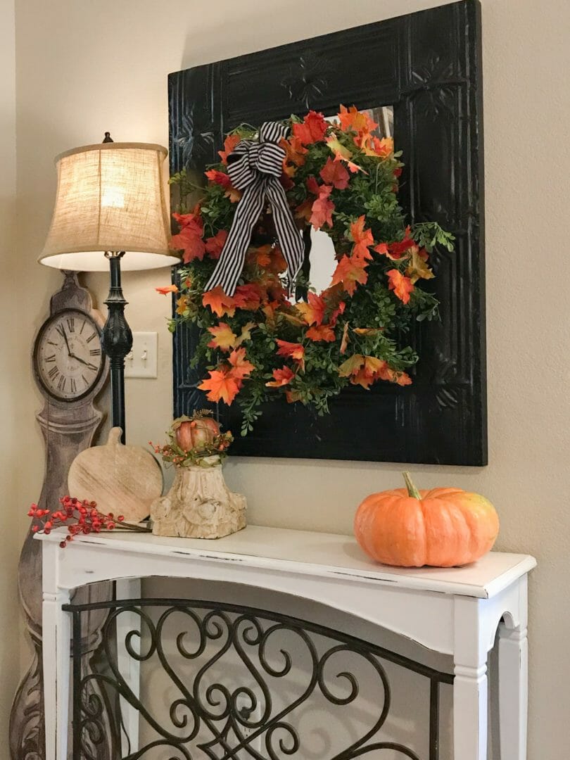 Fall wreath hanging on mirror with pumpkins, lamp and fall decor on console table