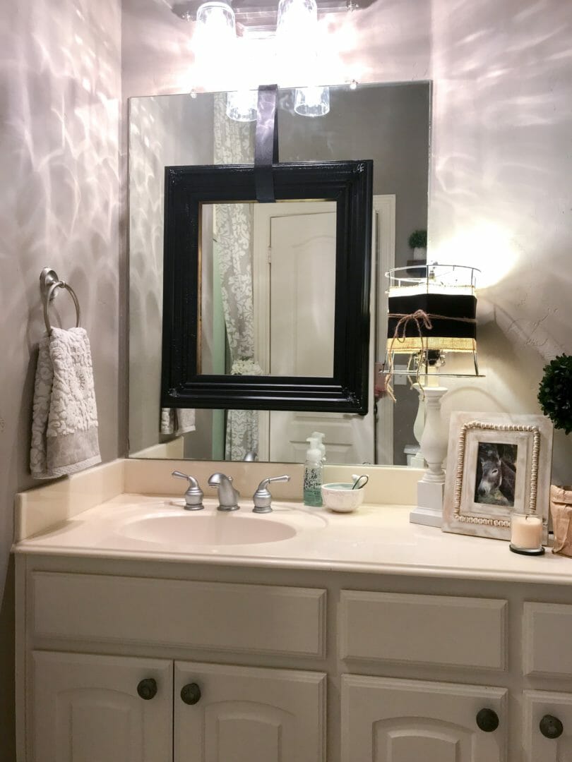 bathroom with black frame over mirror, towel, lamp, frame, candle and soap