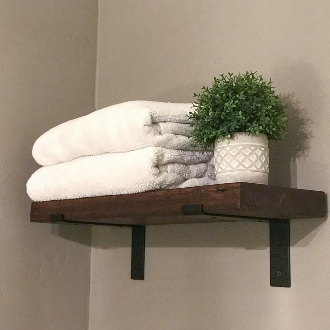 open wood shelf with metal brackets, towels and small accent plant