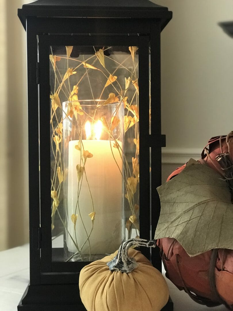 black lantern with lit candle and fall foliage with pumpkins