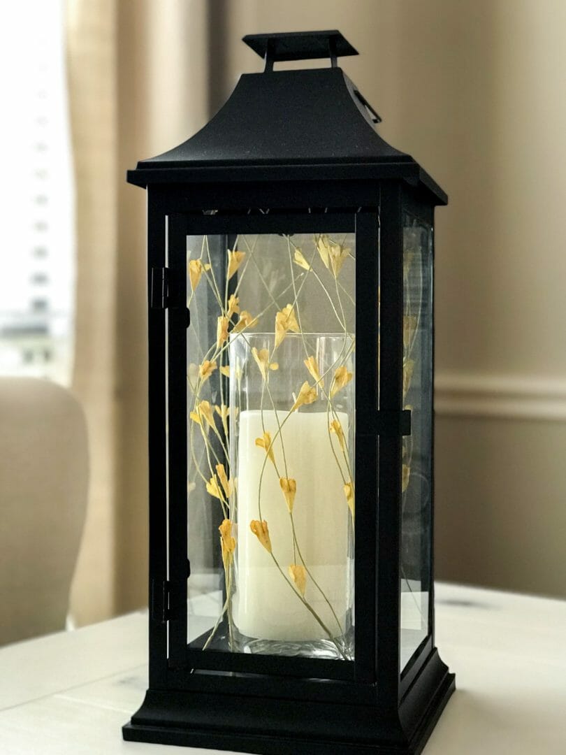 black lantern with candle and yellow fall foliage stems sitting inside lantern