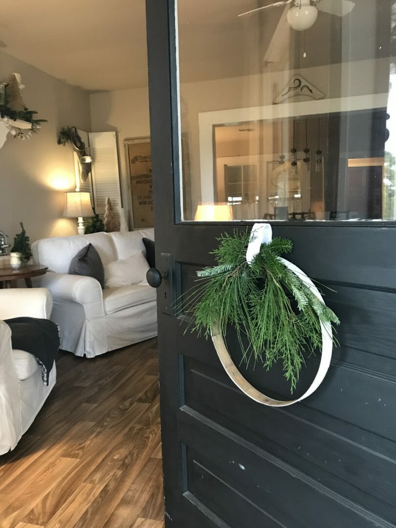 white wood ring wreath on front door with fresh greens and living room in background