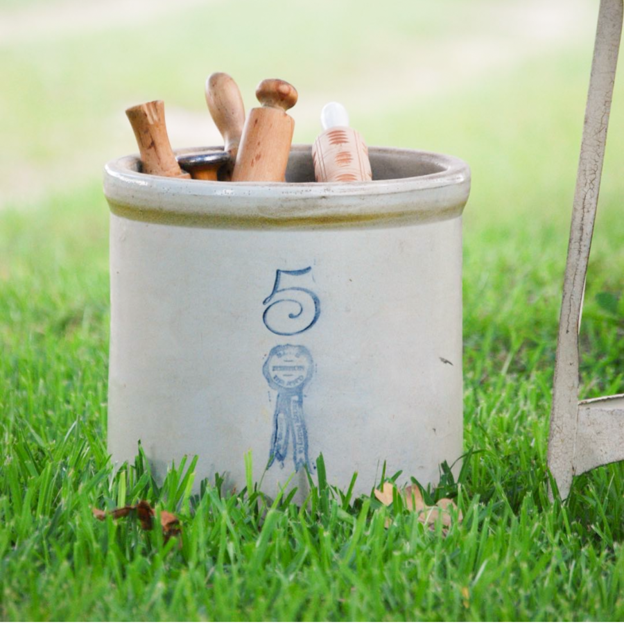 vintage crock with rolling pins sitting in grass