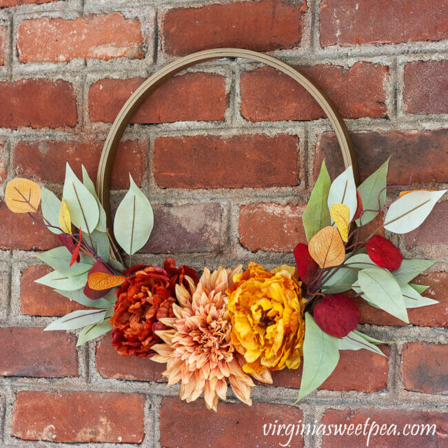hoop wreath with fall flowers hanging on brick wall