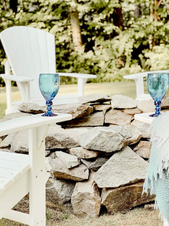 rock fire pit with blue glasses and white chairs