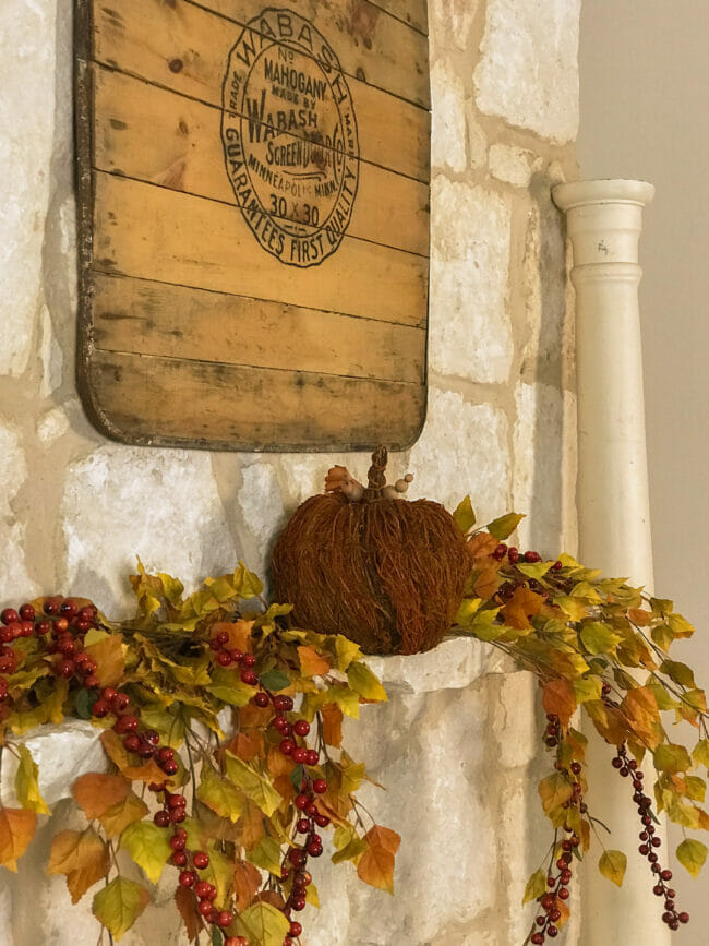 mantel with fall stems and one pumpkin and vintage wooden sign