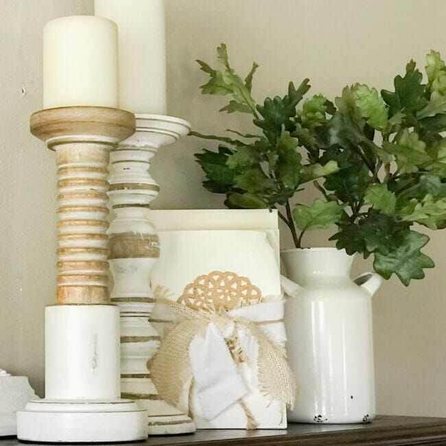 Natural and white candles sticks, deconstructed books and white vase with leafy greenery stems