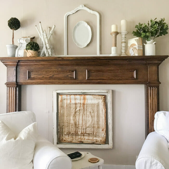 Farmhouse styled mantel with vintage ceiling tin, window frame and white chairs