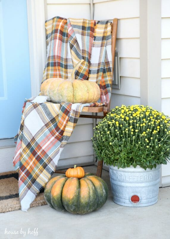 fall porch with chair, plaid blanket, mum and pumpkin sitting in chair