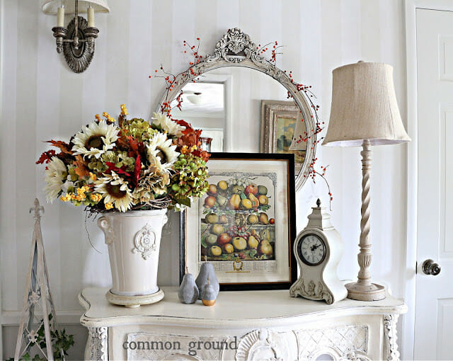 white chest with fall flowers, lamp, mirror and framed fruit picture