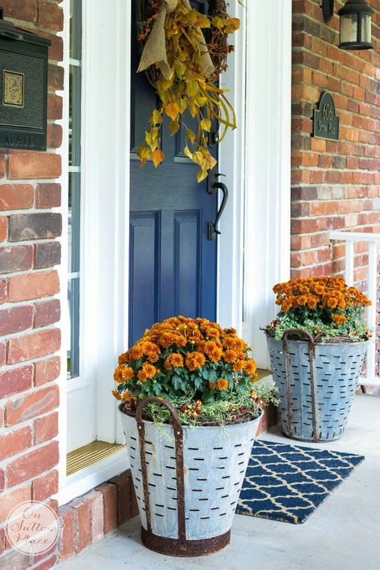two olive buckets with mums and wreath on blue door
