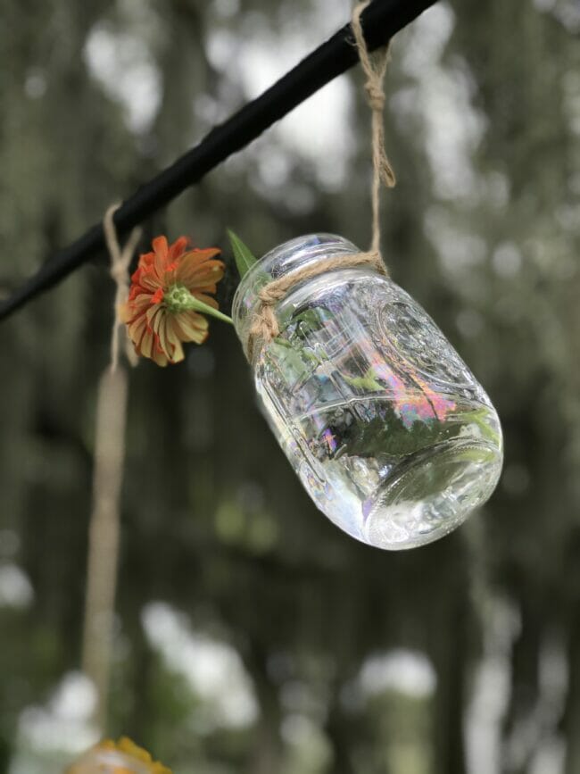 single mason jar with one flower hanging on a rod