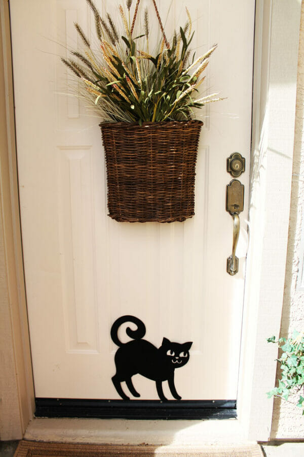 white front door with basket of stems and black cat