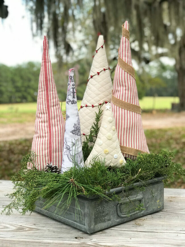 Fabric trees with greenery stems in metal crate on table outdoors