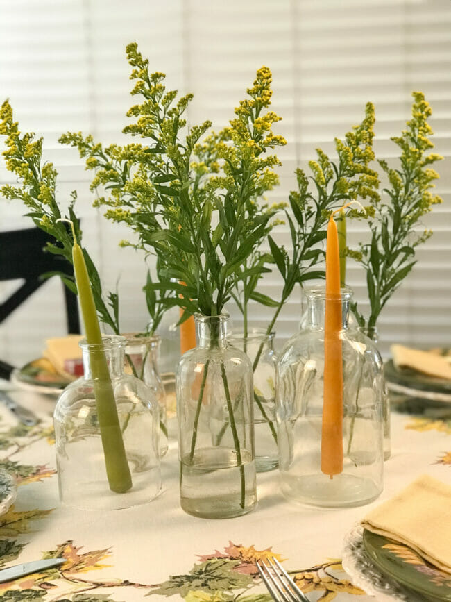 Bottle centerpiece with green and gold candles and flowers