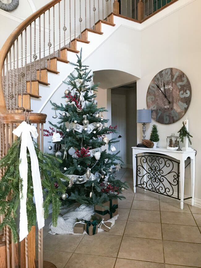 entryway with Christmas tree and bough with white bow on stairway railing