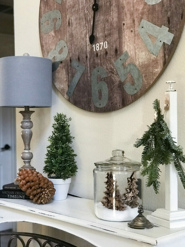 console table with clock, lamp, large pinecone and greenery