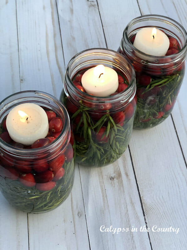 3 mason jars with rosemary and cranberries and floating candles