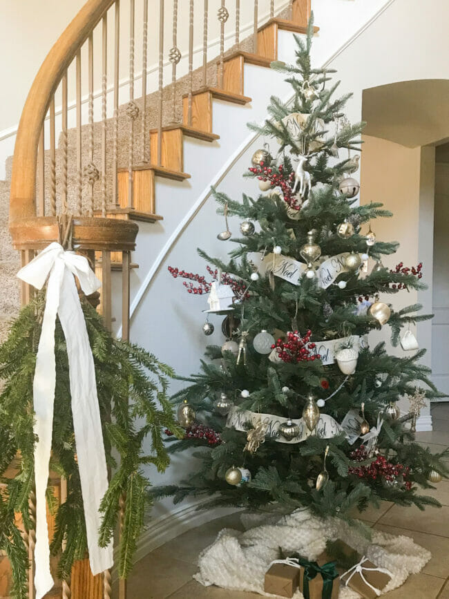 Full Christmas tree in front of stairs with fresh greenery and bow 
