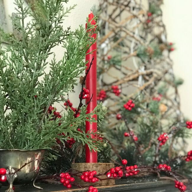 red candle in log with branch greenery in silver creamer
