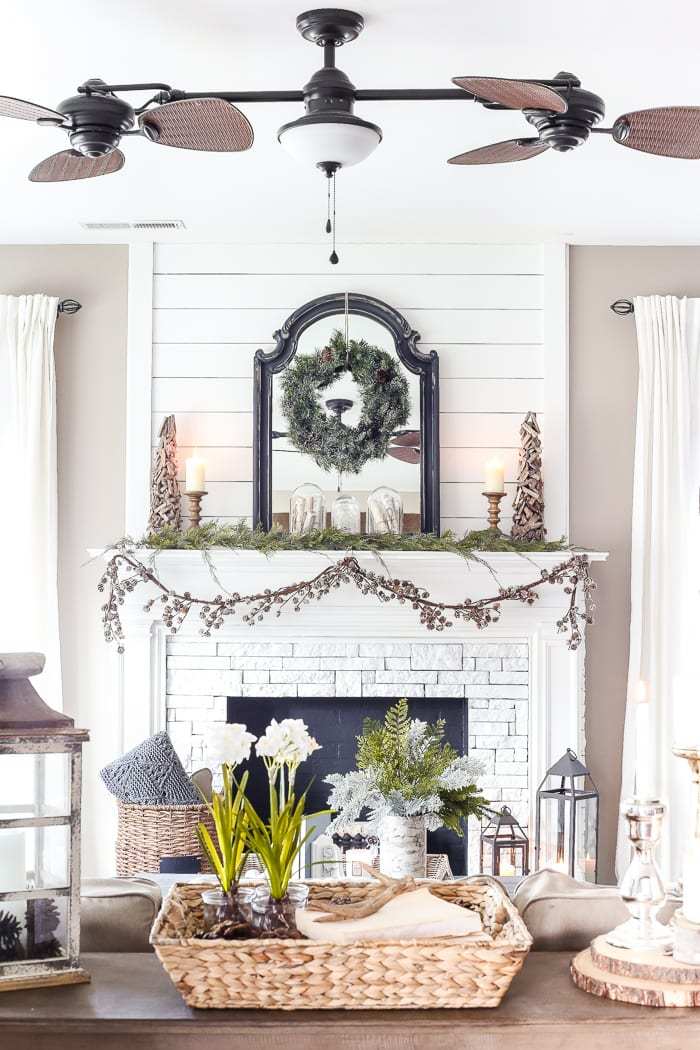 white brick mantle with greenery and cones and a wreath over a mirror