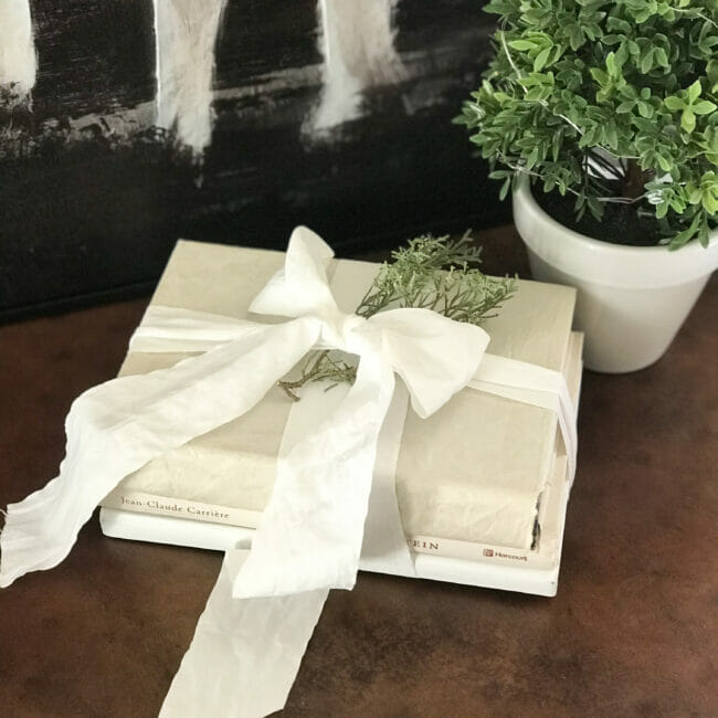 stack of white books with ribbon bow and small piece of greenery tucked in