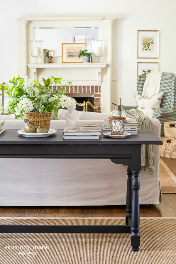 black console table with plant, books, candle and mantel in background
