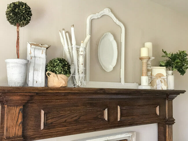 wood mantel with platter inside frame, white spindles inside fencing as vase and candles