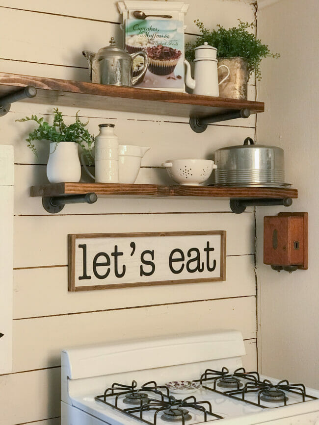 open shelving with white dishes and let's eat sign