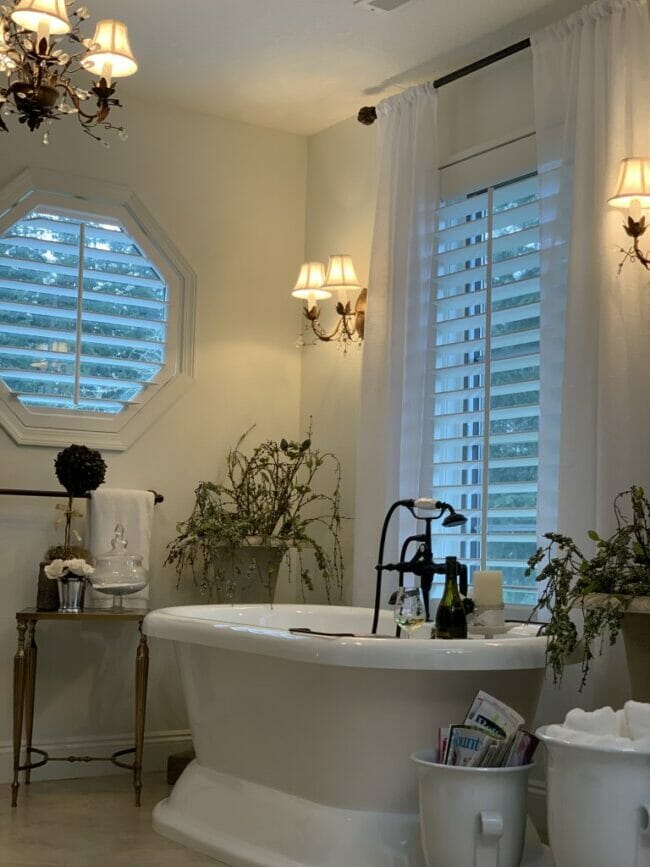 bathtub with sconces on walls by windows and plants 