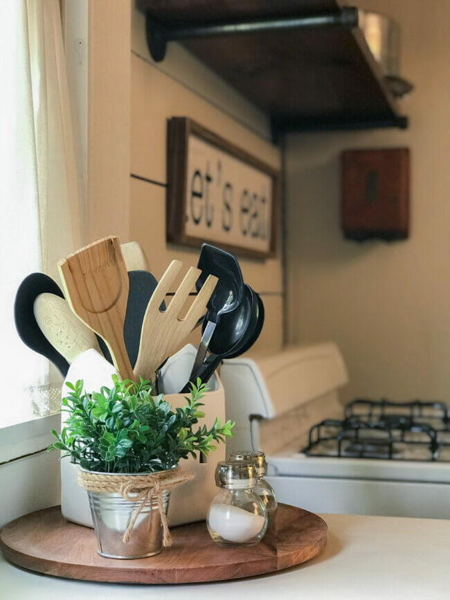 utensils in jar, white oven and greenery on wood tray