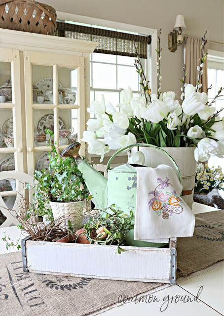 table centerpiece with green watering can, white tulips and other greenery