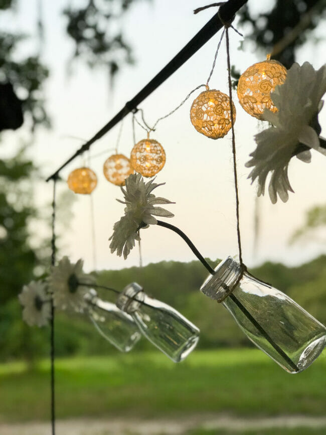 clear bottles with flowers hanging from rod with ball lights