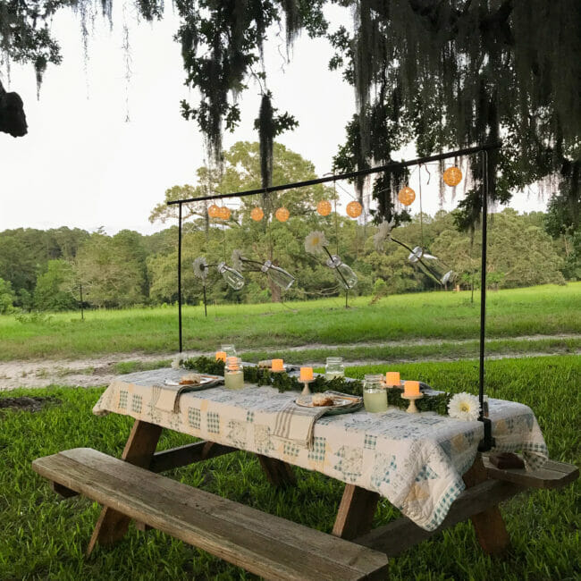 outdoor picnic table with rod, hanging flowers, and candles on a quilt