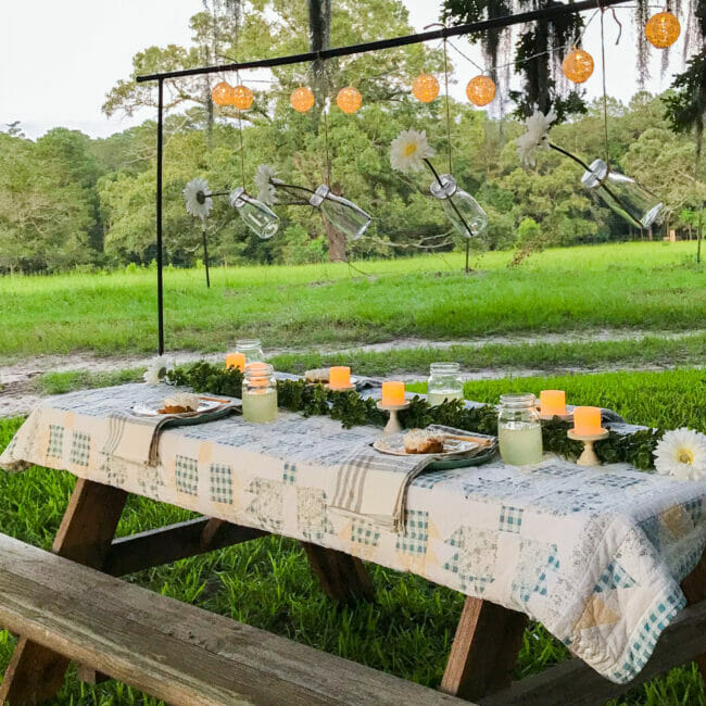 picnic table with vintage quilt and rod with hanging flowers in bottles and lace ball lights