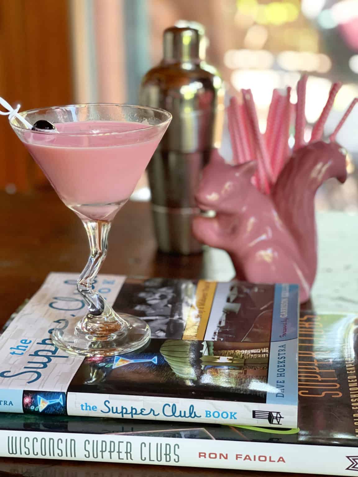 pink squirrel with pink drink sitting onbooks