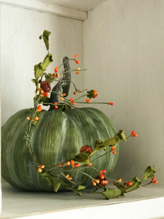 green pumpkin with orange berry mini garland wrapped around it.