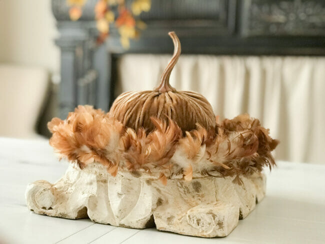 gold pumpkin sitting on a riser inside a feather wreath